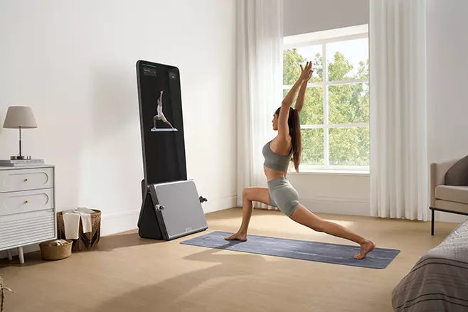 A woman performing a pilates pose while following a workout on a smart fitness mirror at home.